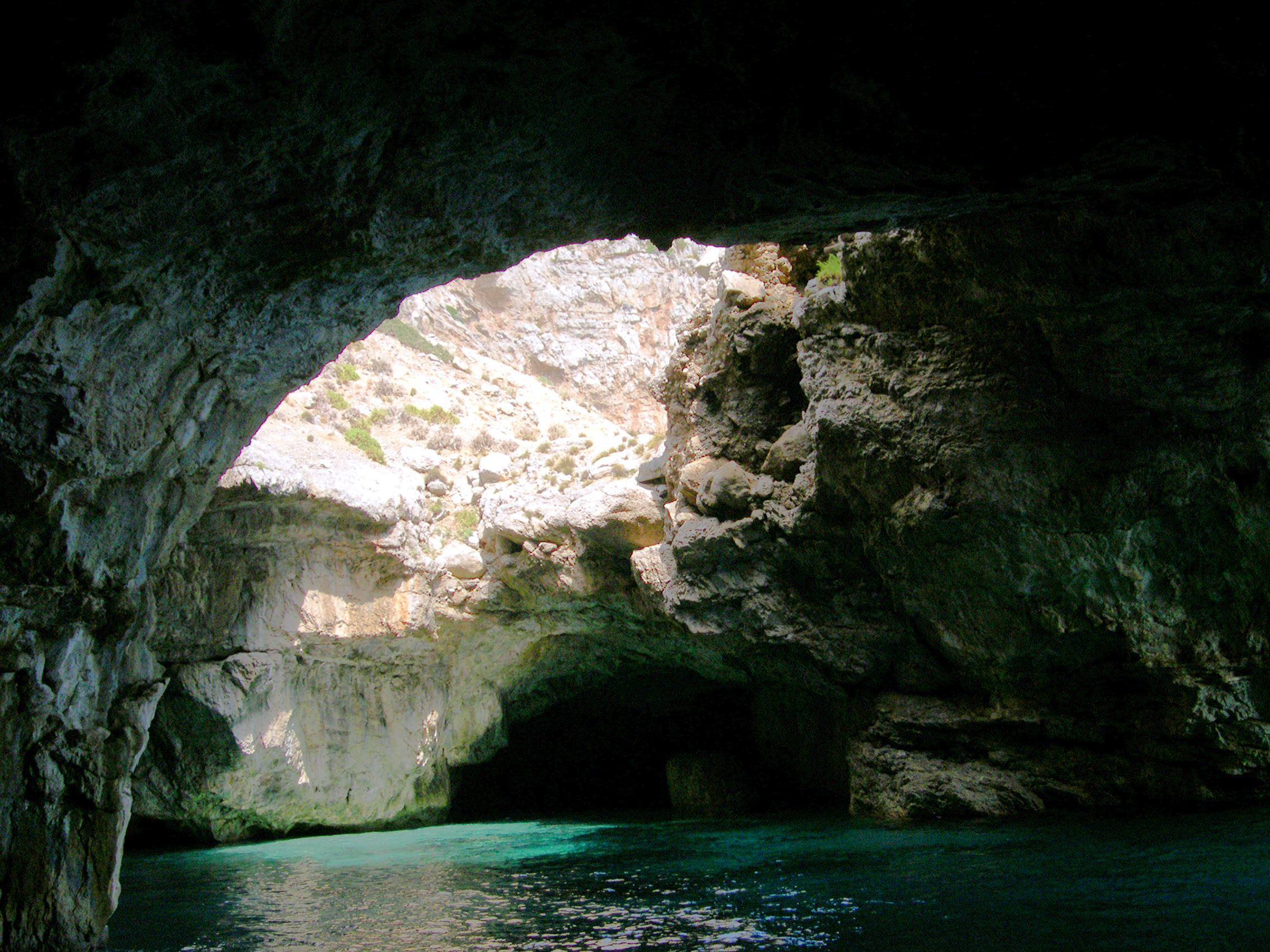 Grotta illuminata con acqua turchese e apertura nella roccia